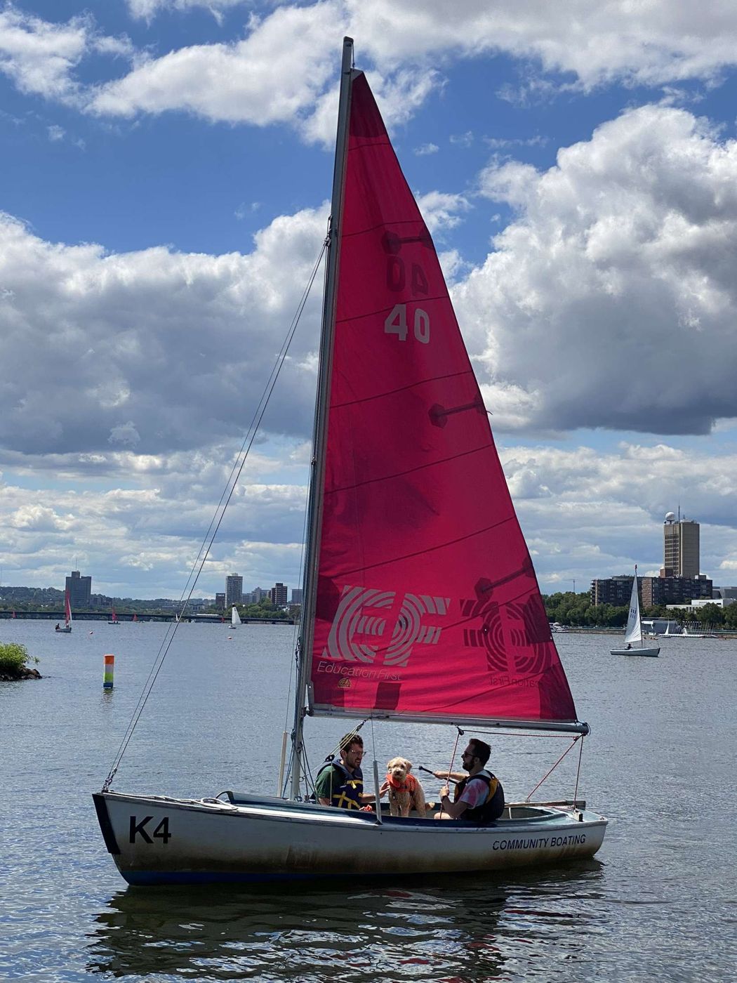 Keelboat with a red sail and crew on the Charles River