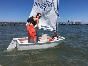 Instructor coaching a young sailor in an Opti